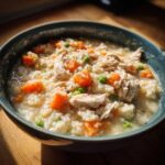 Close-up of a hearty bowl of Instant Pot Creamy Chicken and Rice Soup with visible shredded chicken, carrots, and peas.