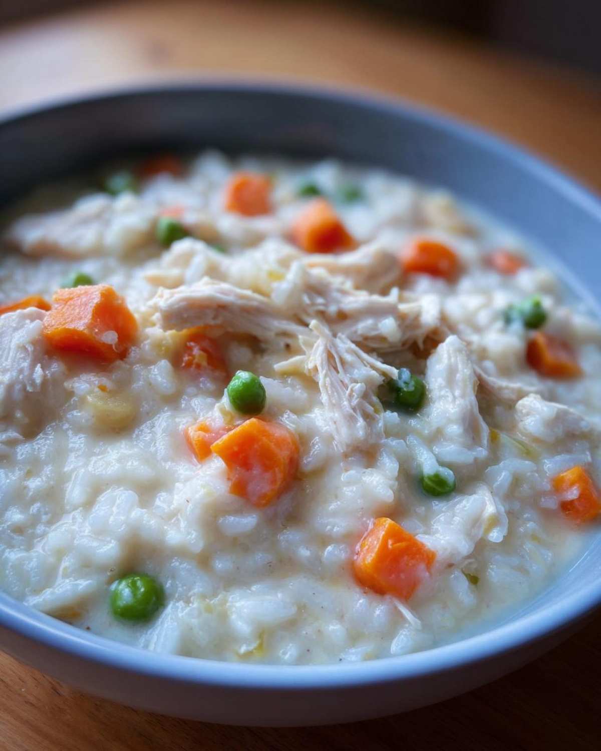 A close-up of a bowl of Instant Pot Creamy Chicken and Rice Soup topped with shredded chicken, carrots, and peas.