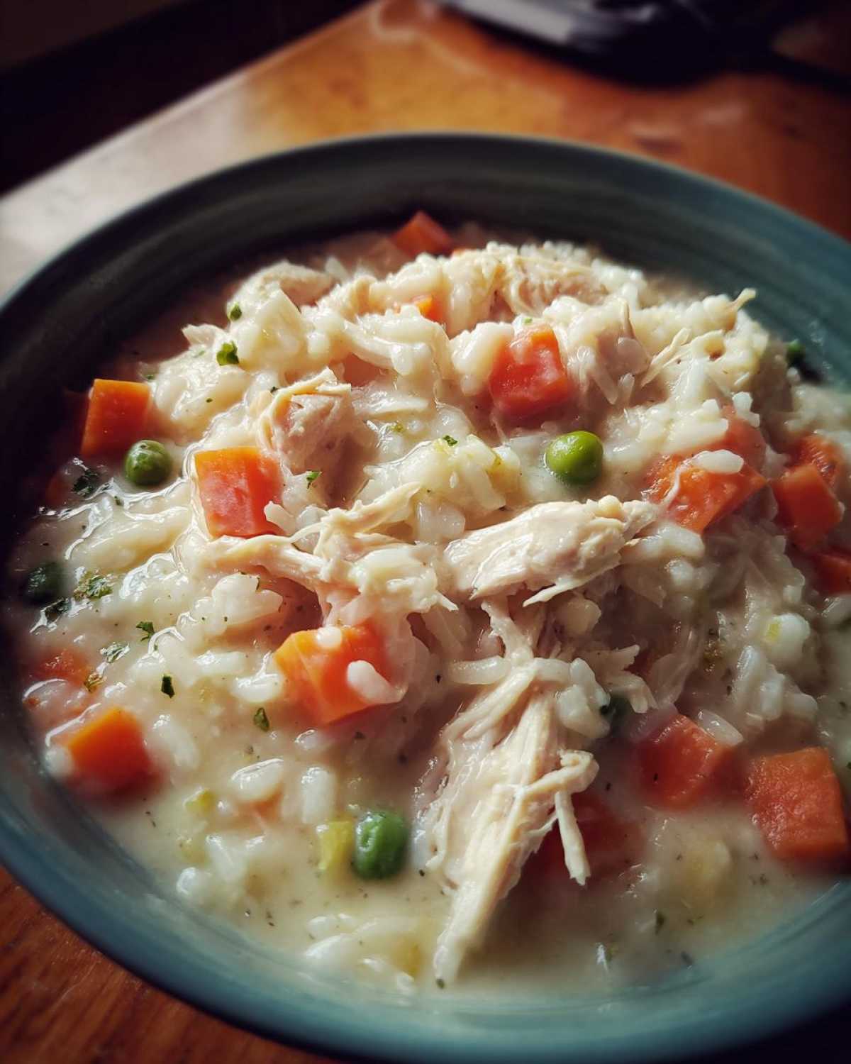 Close-up of a bowl of Instant Pot Creamy Chicken and Rice Soup with shredded chicken, rice, carrots, and peas.