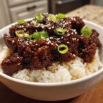A white bowl filled with white rice topped with saucy Instant Pot Korean Beef, garnished with sesame seeds and green onions.