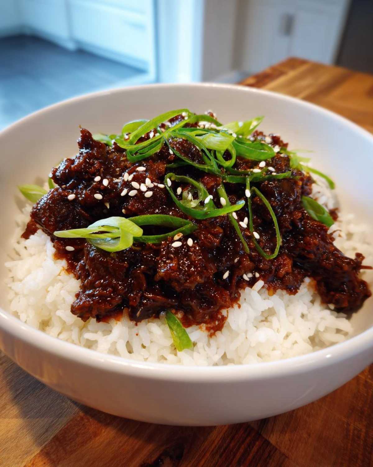 A close-up of Instant Pot Korean Beef and Rice Bowls, featuring saucy beef over white rice, topped with green onions and sesame seeds.