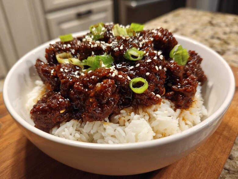 A white bowl filled with white rice topped with saucy Instant Pot Korean Beef, garnished with sesame seeds and green onions.