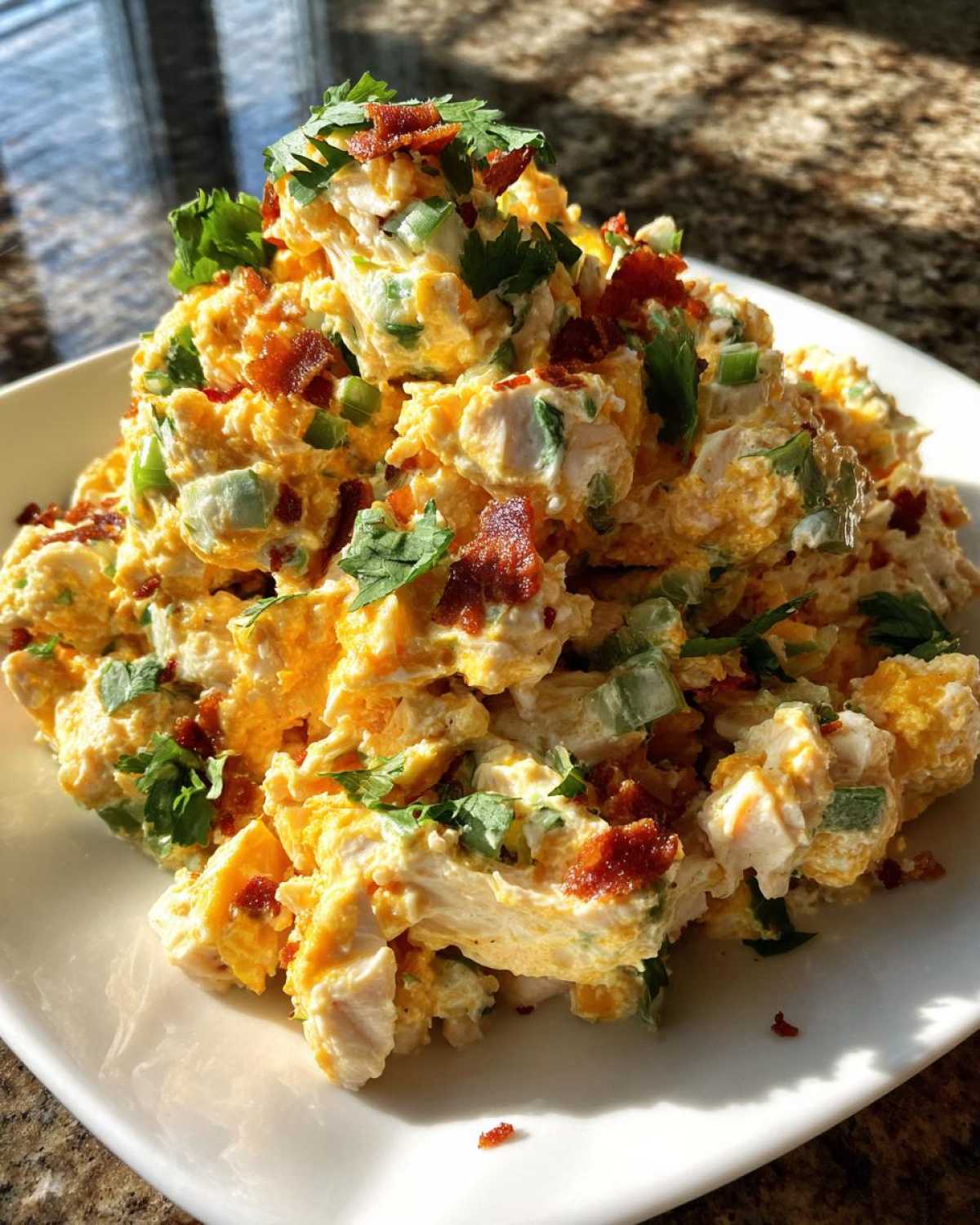 A close-up of a generous serving of jalapeno popper chicken salad topped with bacon crumbles and fresh cilantro.