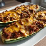 Two halves of zucchini stuffed with seasoned taco meat and topped with melted cheddar cheese, representing Keto Cheesy Taco Stuffed Zucchini Boats.