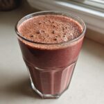 Close-up of a glass filled with a thick, dark red Keto Chocolate Strawberry Smoothie, showing foam on top.