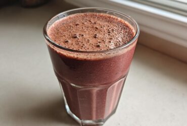 Close-up of a glass filled with a thick, dark red Keto Chocolate Strawberry Smoothie, showing foam on top.