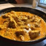 Close-up of Keto Creamy Butter Chicken Skillet simmering in a dark pan, featuring rich orange sauce and seasoned chicken pieces.