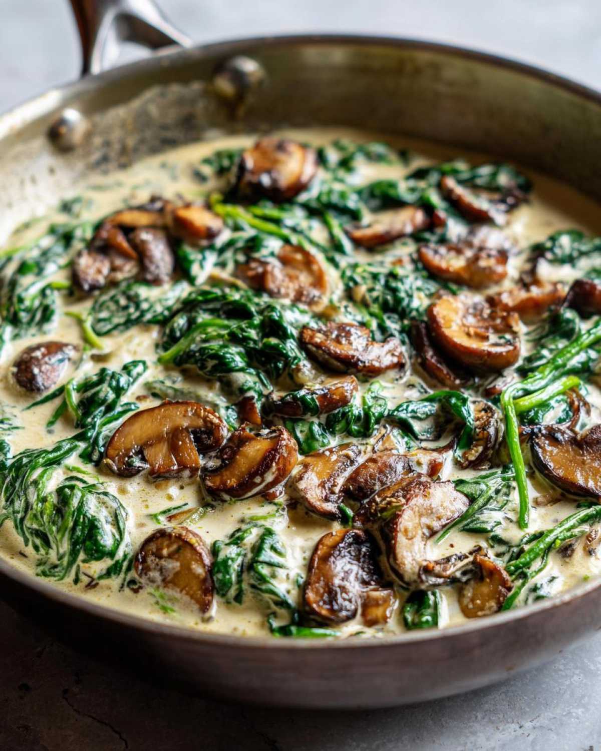 Close-up of Keto Creamy Spinach Mushroom Skillet cooking in a stainless steel pan.