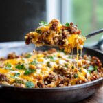 A spoonful of steaming Keto Creamy Taco Skillet with melted cheese being lifted from the cast iron pan.