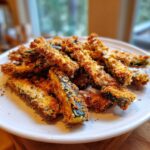 A pile of golden brown, crispy Keto Crispy Parmesan Zucchini Fries served on a white plate.