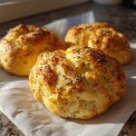 Three golden-brown Keto Everything Bagel Cloud Bread buns sprinkled with seeds and salt, resting on parchment paper.