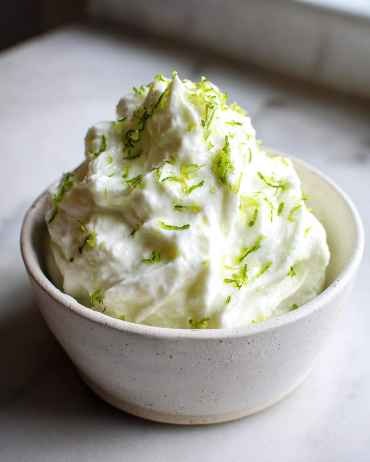 Close-up of a creamy white yogurt dip topped generously with bright green lime zest.