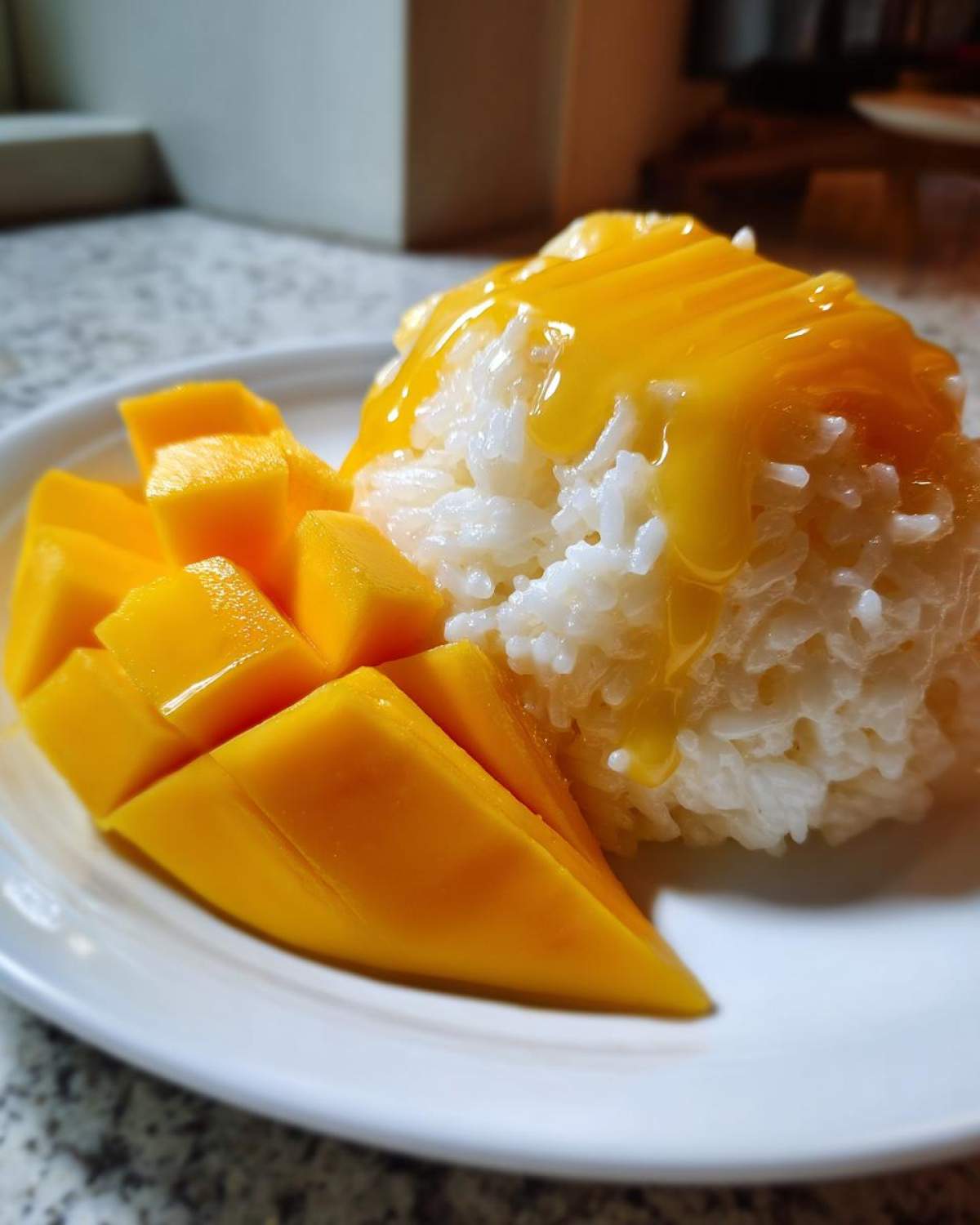 Close-up of a serving of mango sticky rice, featuring sweet white rice topped with mango sauce and fresh, sliced mango.