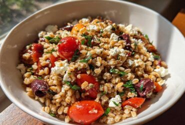 A close-up bowl of vibrant Mediterranean farro salad featuring whole farro grains, cherry tomatoes, Kalamata olives, and crumbled feta cheese.