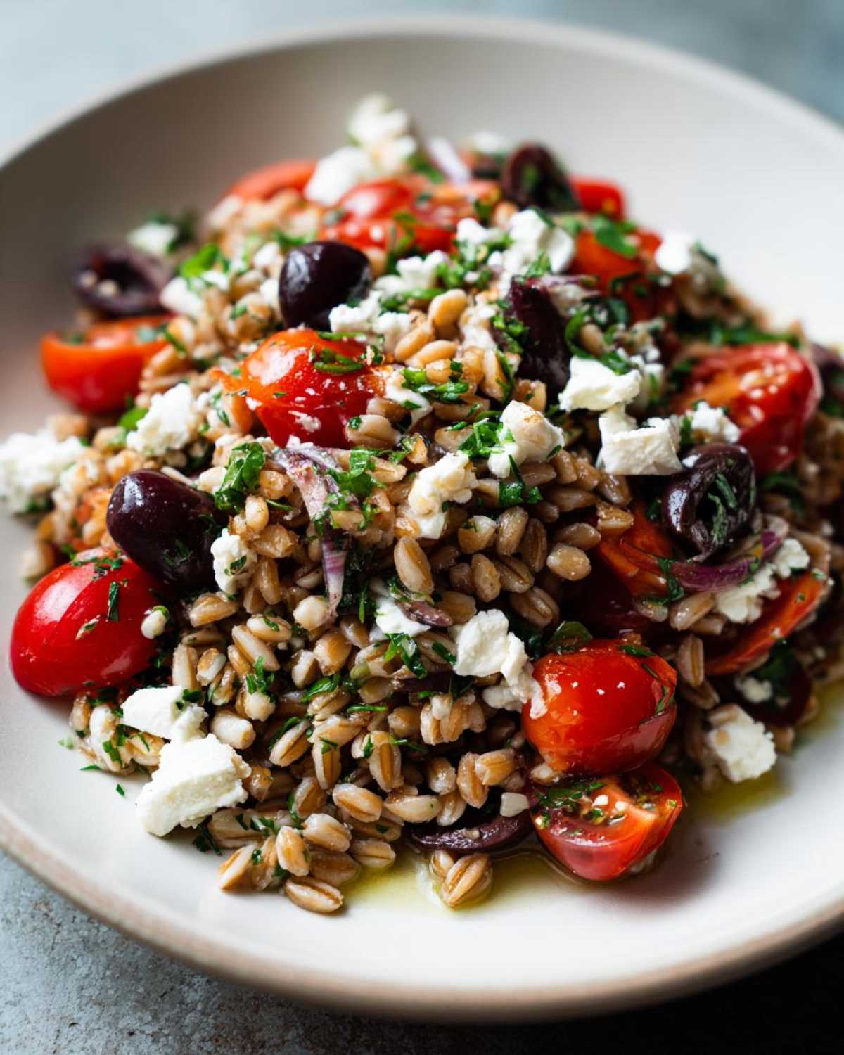 Close-up of a bowl filled with Mediterranean farro salad featuring plump farro grains, cherry tomatoes, Kalamata olives, and crumbled feta cheese.