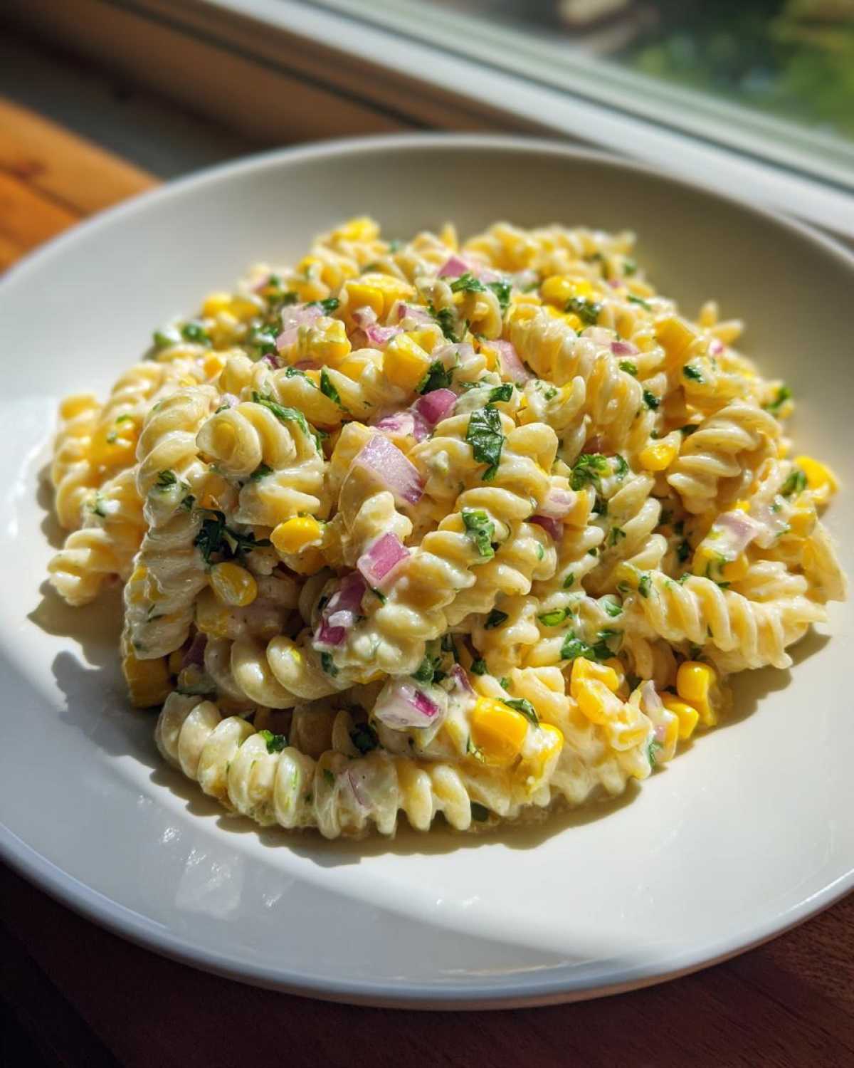 A close-up of Mexican Street Corn Pasta Salad featuring fusilli pasta, bright yellow corn, and diced red onion in a creamy sauce.
