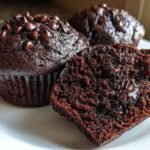 Close-up of moist chocolate muffins, one cut open revealing a rich, dark interior with melted chocolate chips. Perfect chocolate muffins.