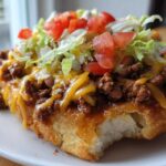 Close-up of a delicious Navajo Taco Fry Bread topped with seasoned ground beef, melted cheese, lettuce, and diced tomatoes.