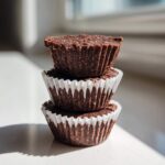 A stack of three rich, dark No-Bake Chocolate Coconut Protein Cups in white paper liners.
