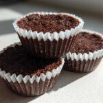 Three rich, dark No-Bake Chocolate Coconut Protein Cups stacked slightly on a white surface.