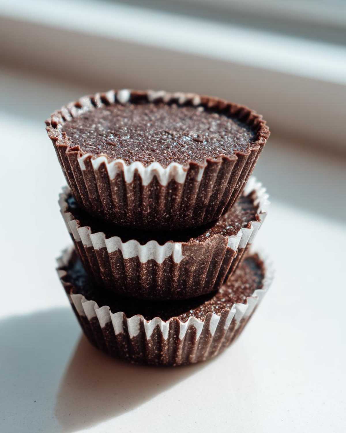 Three dark chocolate No-Bake Chocolate Coconut Protein Cups stacked vertically in white paper liners.