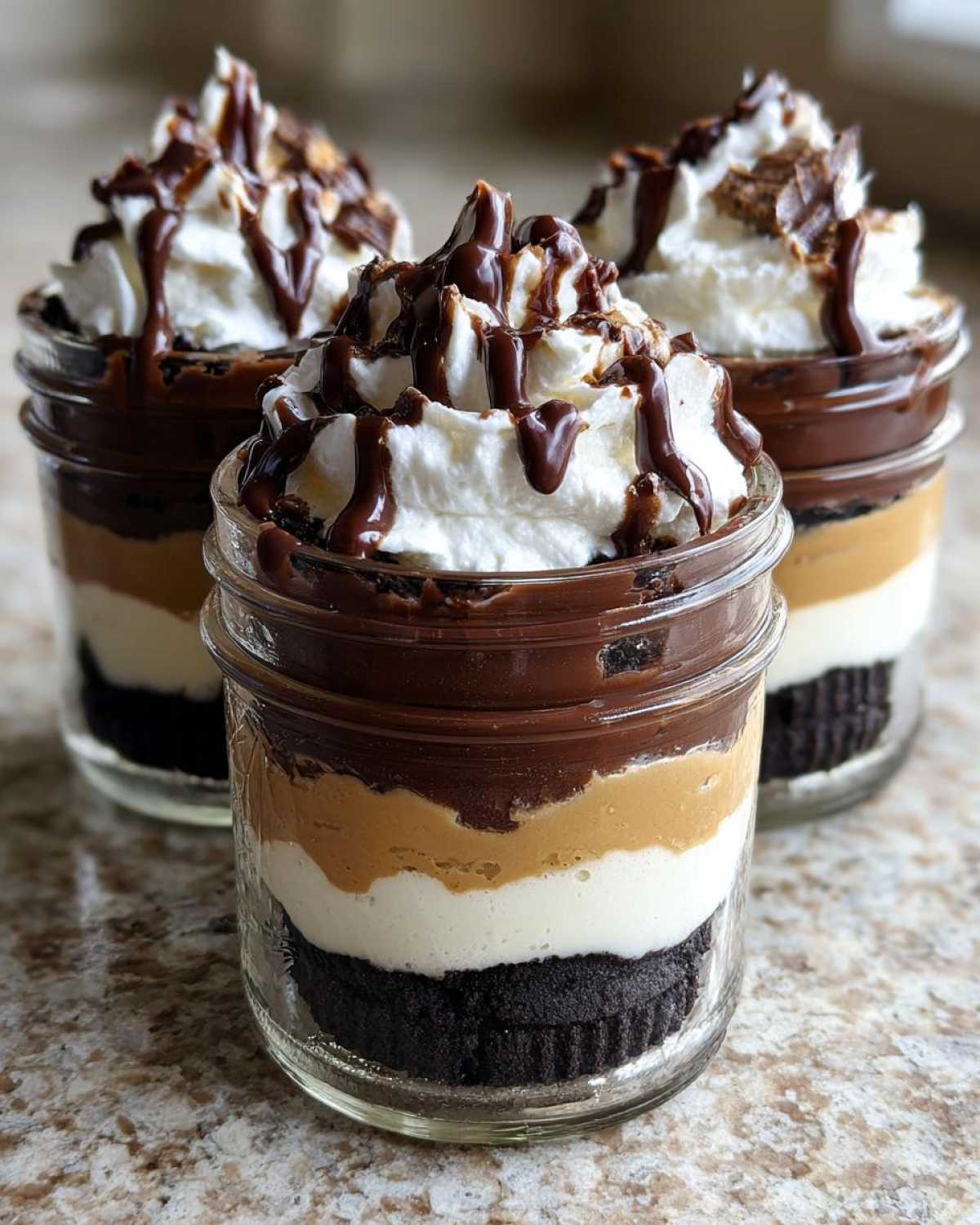 Three individual No-Bake Chocolate Peanut Butter Pie Jars layered with crust, cream, peanut butter, chocolate, and topped with whipped cream and drizzle.