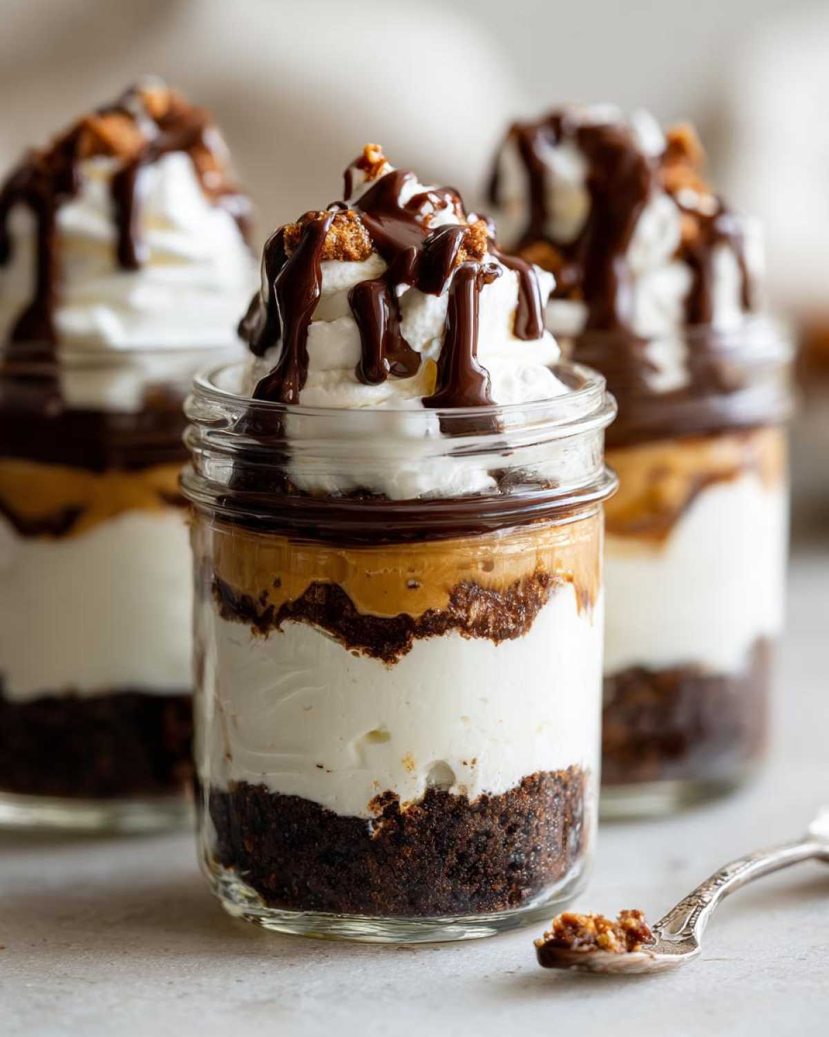 Close-up of one of the No-Bake Chocolate Peanut Butter Pie Jars, showing layers of crust, cream, peanut butter, and whipped topping with chocolate drizzle.