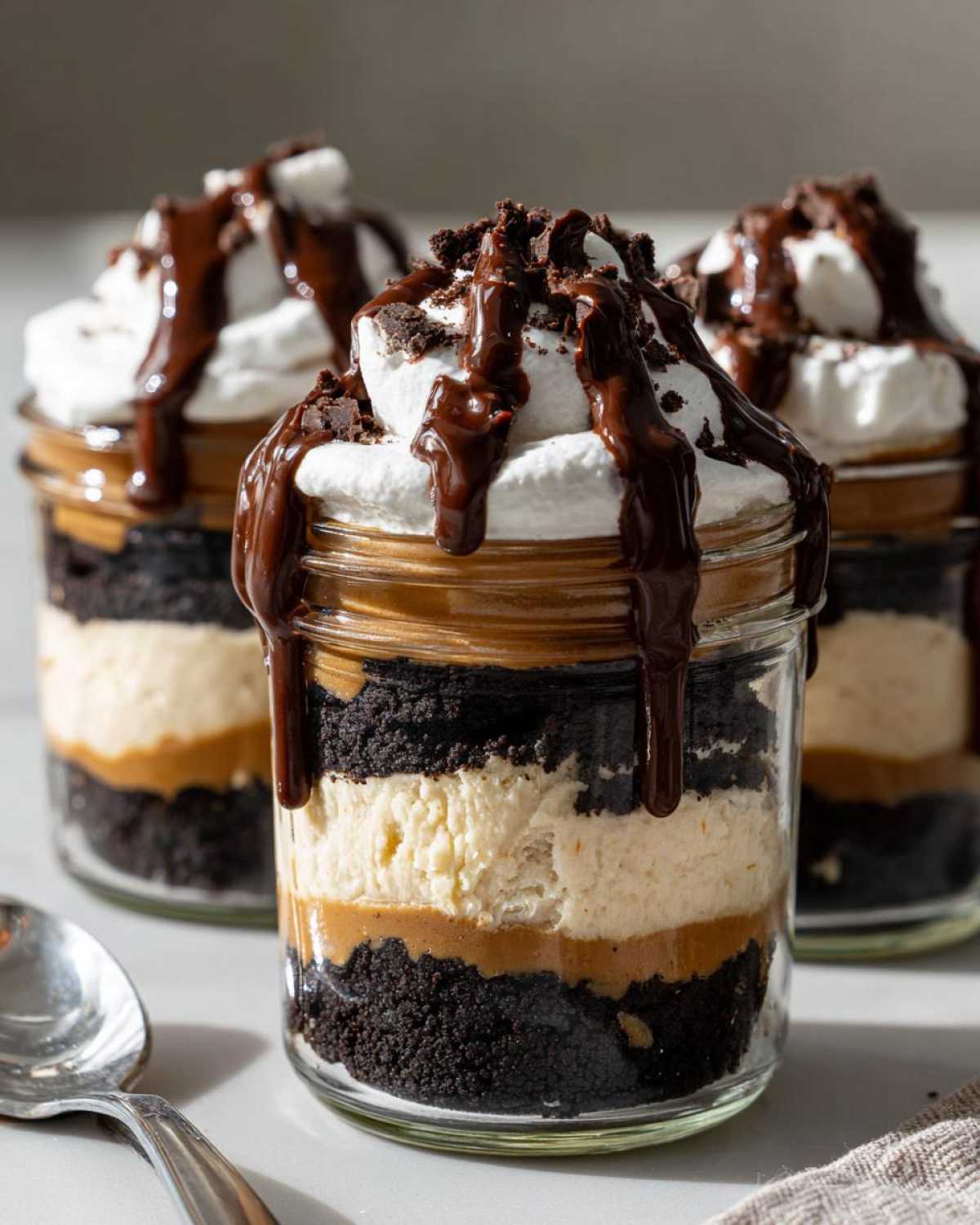 Close-up of layered No-Bake Chocolate Peanut Butter Pie Jars topped with whipped cream and chocolate drizzle.