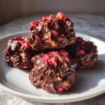 Close-up of four No-Bake Chocolate Strawberry Yogurt Clusters coated in dark chocolate and topped with dried strawberries.