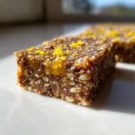 A close-up, macro shot of a single No-Bake Lemon Almond Date Bar showing texture of dates, nuts, and lemon zest topping.