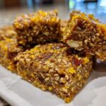 Close-up of several dense, chewy No-Bake Lemon Almond Date Bars packed with nuts and seeds, topped with lemon zest.