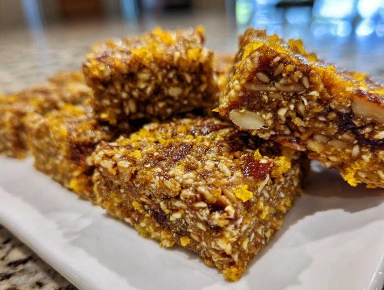 Close-up of several dense, chewy No-Bake Lemon Almond Date Bars packed with nuts and seeds, topped with lemon zest.