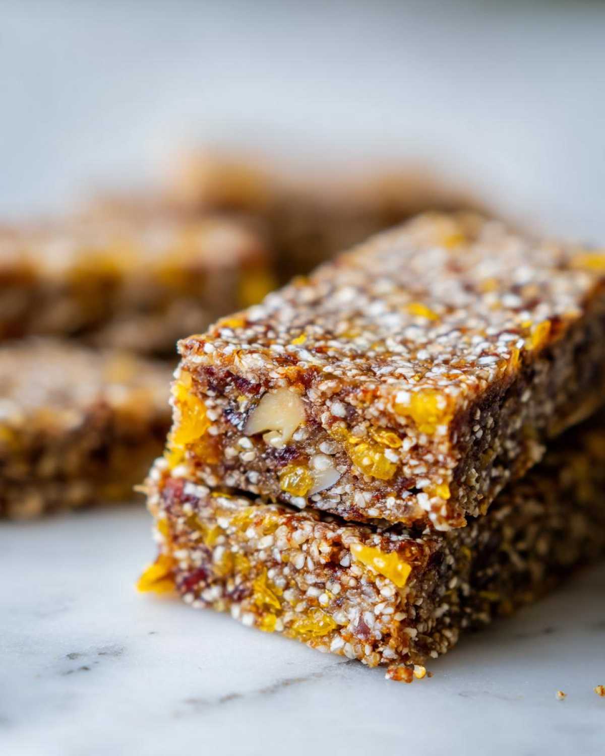 A close-up stack of two No-Bake Lemon Almond Date Bars showing texture from seeds, nuts, and dried fruit.