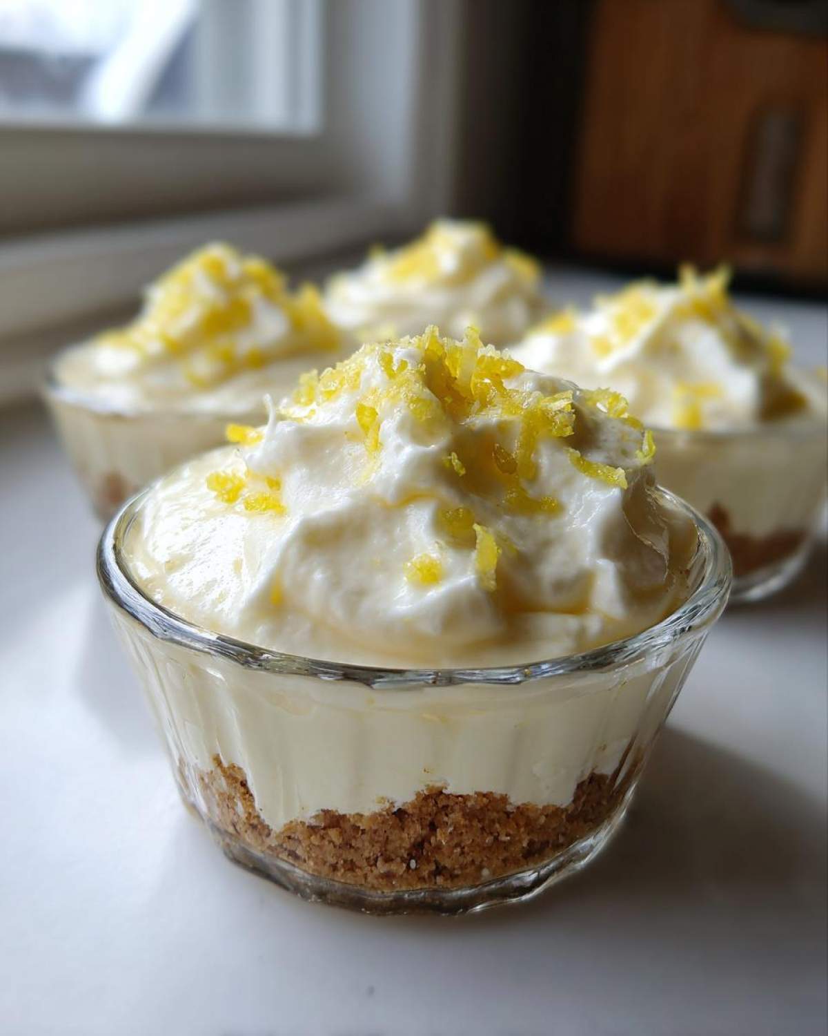 A close-up of one of the No-Bake Lemon Cream Pie Cups, showing the graham cracker crust, creamy filling, and lemon zest topping.