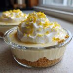 Two individual No-Bake Lemon Cream Pie Cups featuring a graham cracker crust, lemon filling, and whipped cream topped with bright yellow lemon zest.