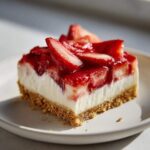 Close-up of a square slice of No Bake Spring Strawberry Dessert with a graham cracker crust, creamy white layer, and glossy strawberry topping.