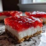 A close-up, cross-section view of a single serving of No-Bake Strawberry Pretzel Dessert Bars showing the pretzel crust, cream cheese layer, and strawberry gelatin topping.