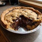 A close-up of a Nutella Scoopable Cookie Pie with a slice removed, showing the molten, gooey chocolate filling.