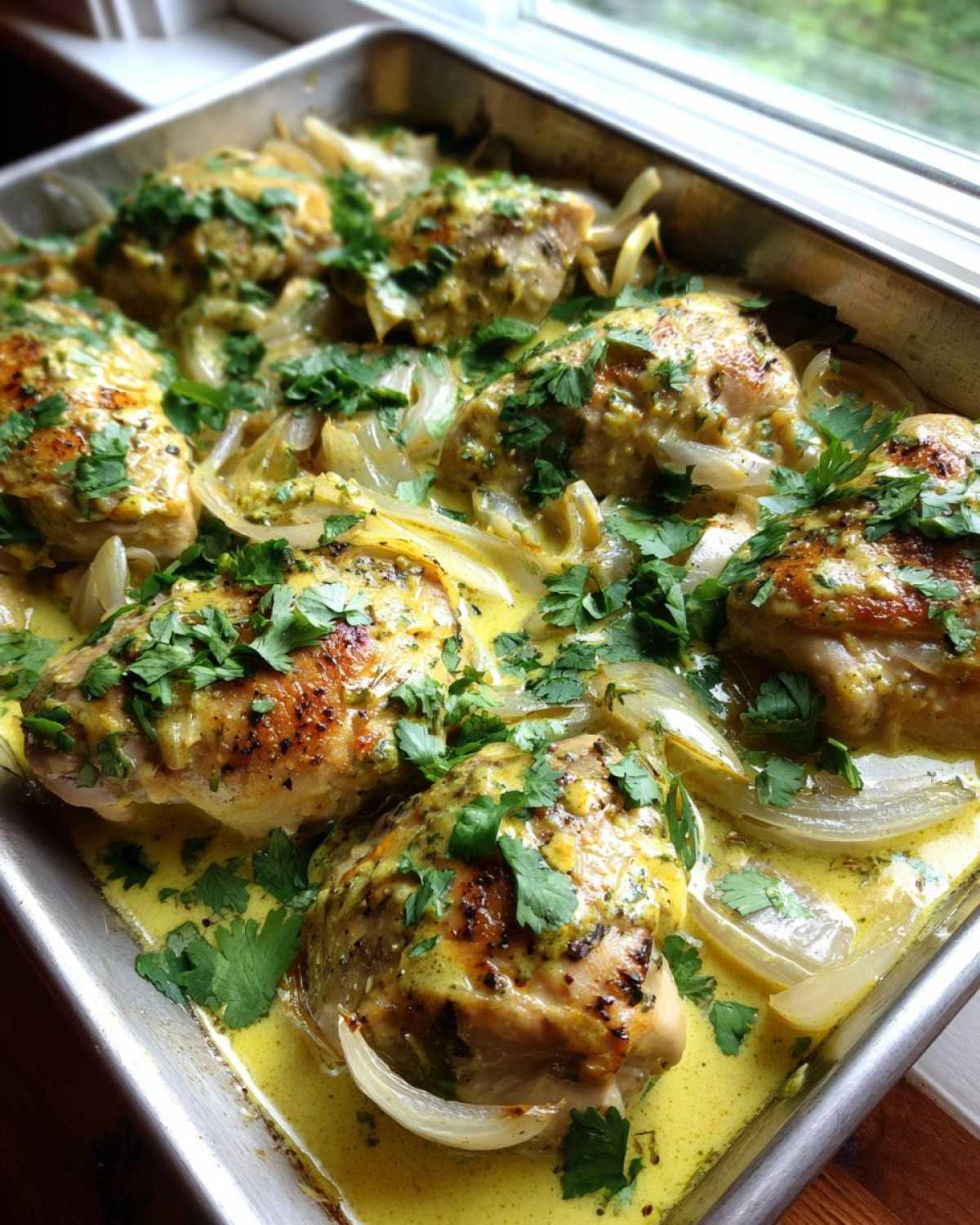 Close-up of One-Pan Creamy Coconut Lime Chicken thighs baked with onions in a yellow sauce, garnished with fresh cilantro.