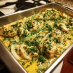 Close-up of One-Pan Creamy Coconut Lime Chicken pieces simmering in a rich, yellow coconut sauce with onions and fresh parsley.