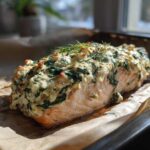 A baked fillet of One-Pan Creamy Spinach Feta Stuffed Salmon on parchment paper, topped with herbs.