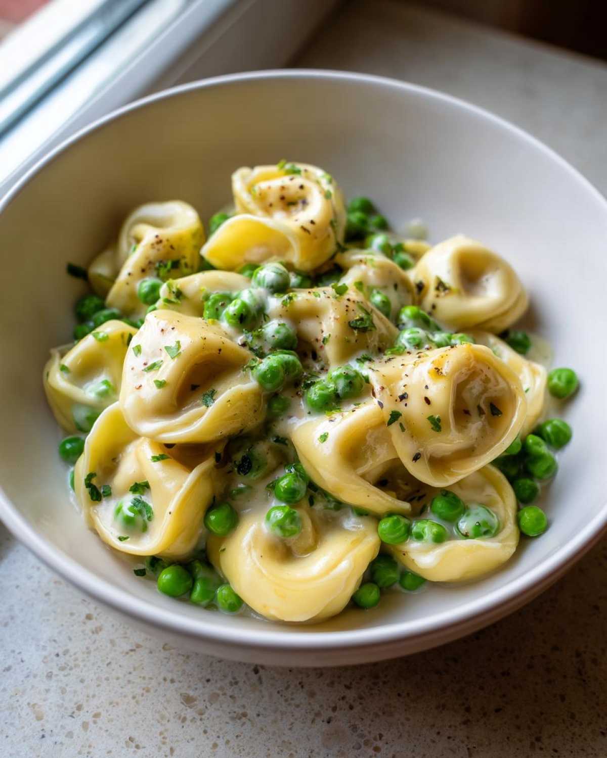 A close-up of One-Pot Creamy Garlic Butter Tortellini and Peas served in a white bowl, topped with pepper and parsley.