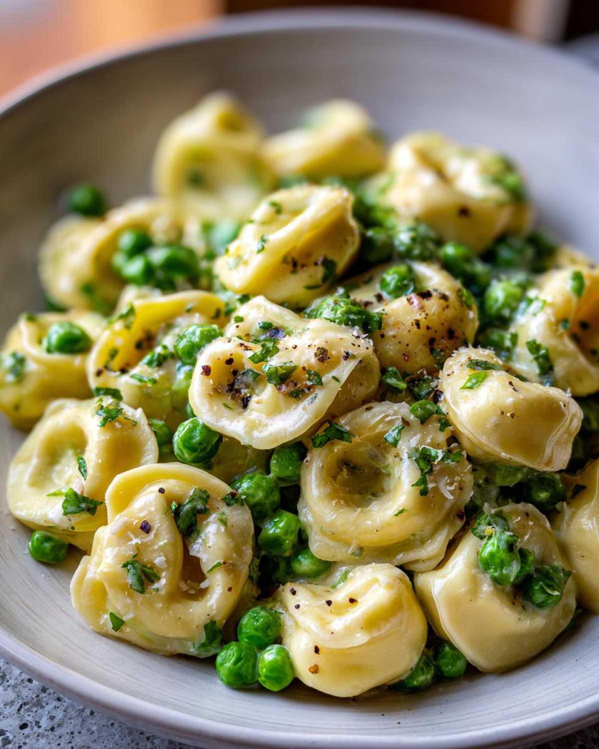 Close-up of One-Pot Creamy Garlic Butter Tortellini and Peas garnished with parsley and pepper.