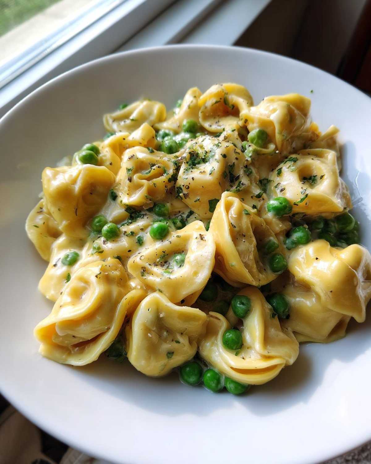 Close-up of One-Pot Creamy Garlic Butter Tortellini and Peas served in a white bowl, topped with herbs.