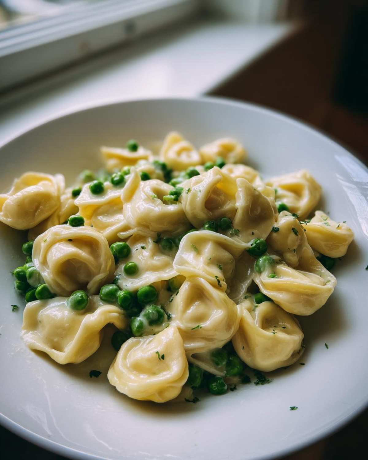 Close-up of One-Pot Creamy Garlic Butter Tortellini and Peas served in a white bowl, garnished with parsley.