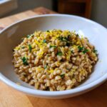 A close-up of One-Pot Creamy Lemon Garlic Farro topped with bright yellow lemon zest and fresh parsley in a white bowl.