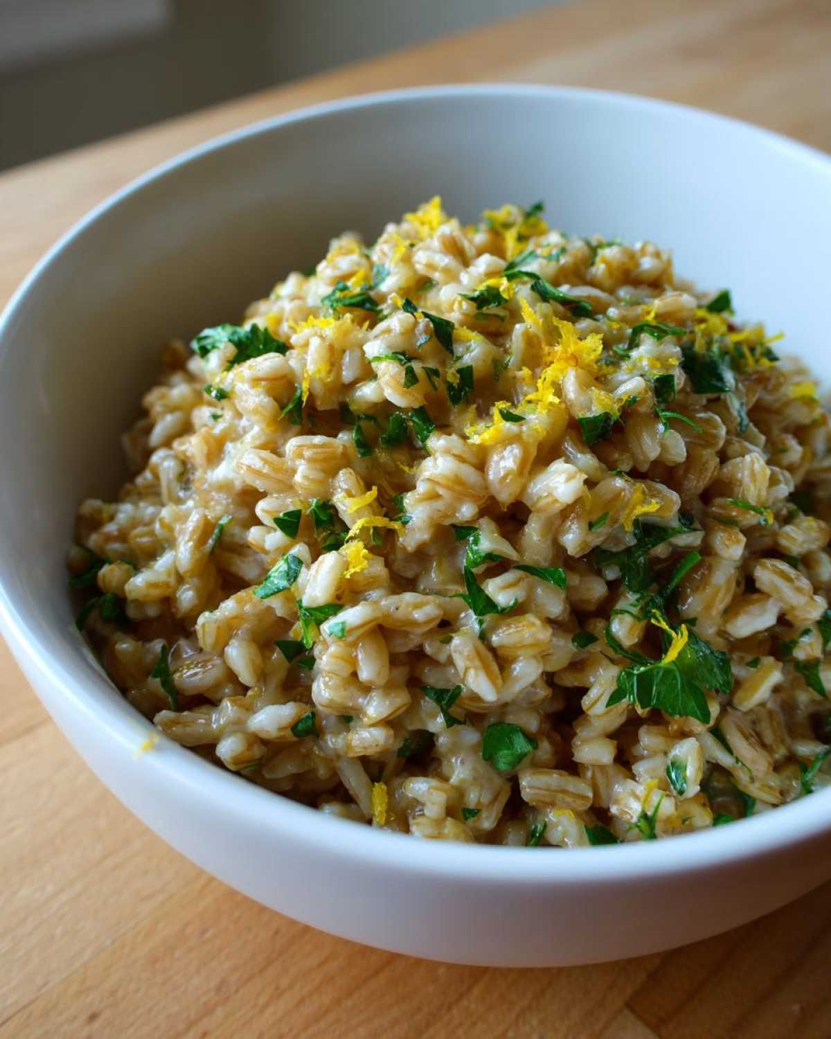 A close-up of One-Pot Creamy Lemon Garlic Farro topped with bright lemon zest and fresh parsley in a white bowl.