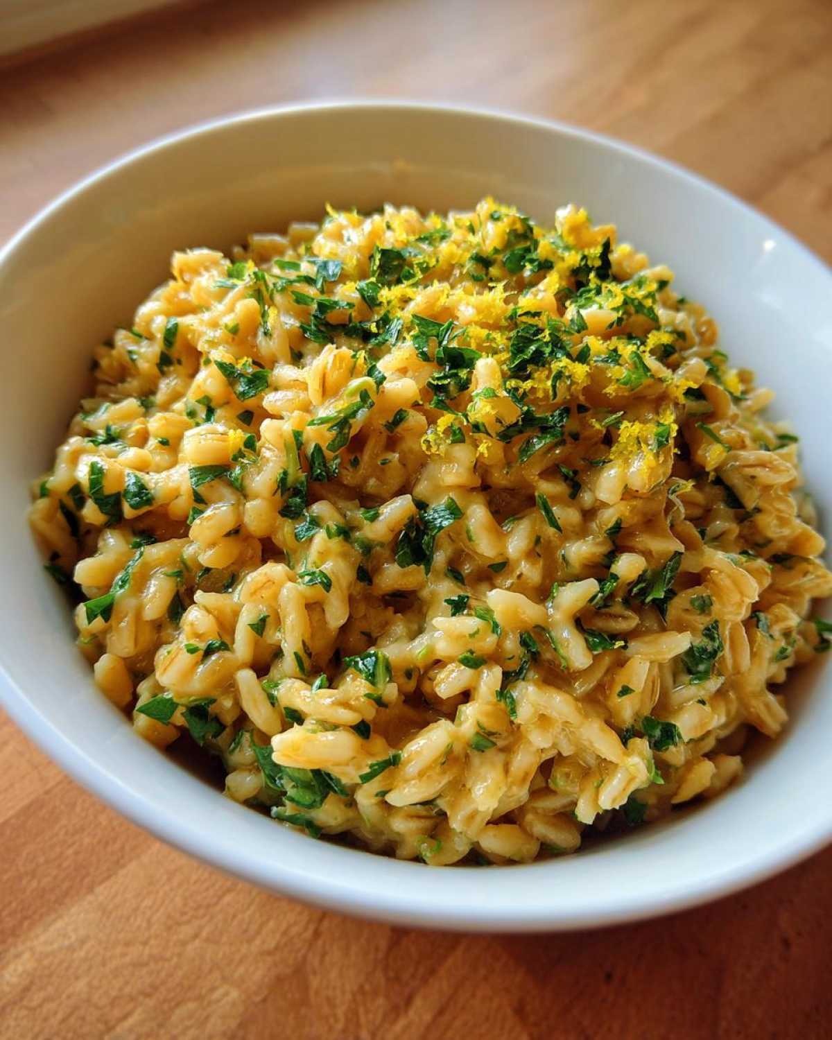 A close-up of One-Pot Creamy Lemon Garlic Farro topped with fresh parsley and bright yellow lemon zest.