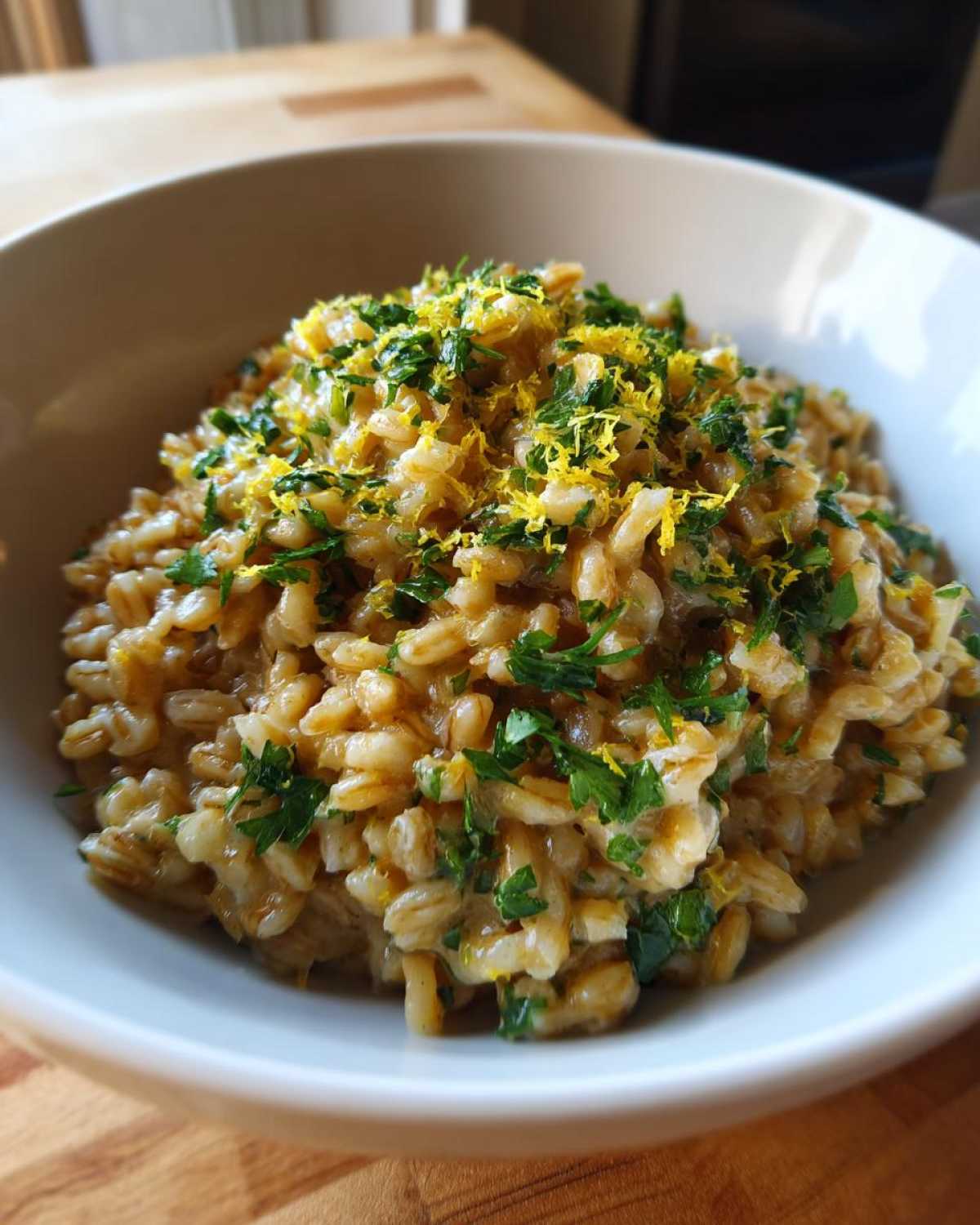 Close-up of a bowl of One-Pot Creamy Lemon Garlic Farro topped with bright yellow lemon zest and fresh chopped parsley.