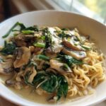 A close-up of One-Pot Creamy Mushroom Spinach Ramen featuring ramen noodles, sliced mushrooms, and wilted spinach in a creamy sauce.